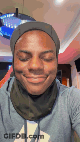 A Man Wearing A Hooded Sweatshirt And A Scarf Around His Neck Smiles With His Eyes Closed GIF