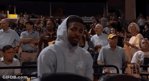 A Man Wearing A Hooded Sweatshirt Is Standing In Front Of A Crowd Of People At A Basketball Game . GIF