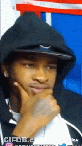 A Man Wearing A Hoodie And A Hat Is Thinking With His Hand On His Chin GIF