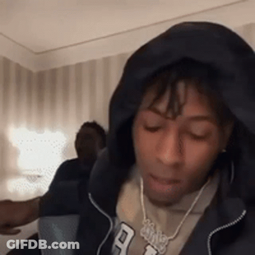 A Man Wearing A Hoodie And A Necklace Is Sitting In A Room With His Eyes Closed . GIF