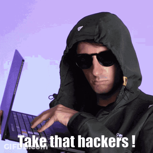 A Man Wearing A Hoodie And Sunglasses Is Typing On A Laptop With The Words Take That Hackers Written Below Him GIF