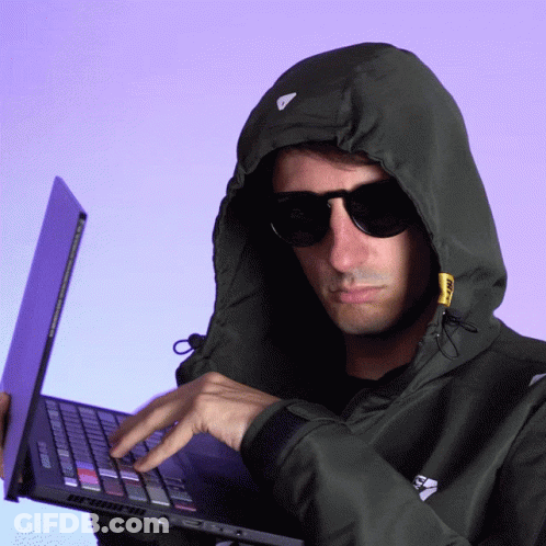 A Man Wearing A Hoodie And Sunglasses Is Typing On His Laptop GIF