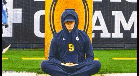 A Man Wearing A Hoodie Is Sitting In A Lotus Position On A Field . GIF