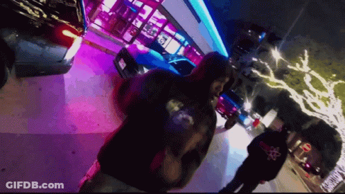 A Man Wearing A Hoodie With A Skull And Crossbones On The Back Walks Down A Street At Night GIF