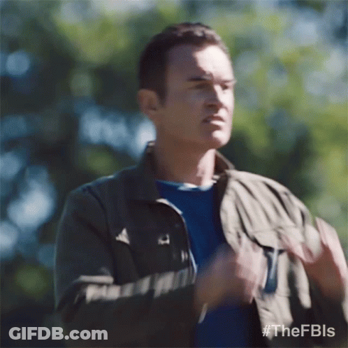 A Man Wearing A Jacket And A Blue Shirt Is Standing In The Woods And Making A Funny Face . GIF