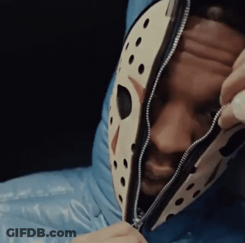 A Man Wearing A Jason Voorhees Mask Is Laying In A Blue Sleeping Bag . GIF