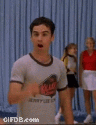 A Man Wearing A Jerry Lee Lip T-Shirt Is Standing In Front Of A Blue Curtain . GIF