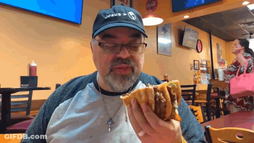 A Man Wearing A Jesus Hat Is Eating A Hamburger GIF