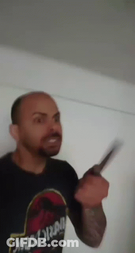 A Man Wearing A Jurassic Park Shirt Is Holding A Knife In His Hand . GIF