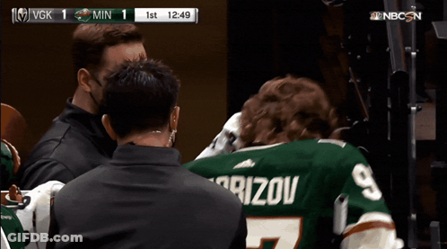 A Man Wearing A Kaprizov Jersey Is Being Escorted By A Man Wearing A Mask GIF
