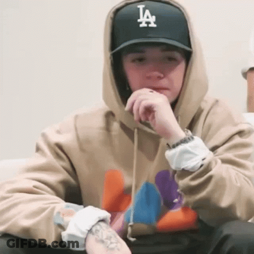 A Man Wearing A La Hat And A Hoodie Is Sitting On A Couch GIF