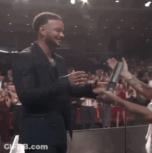 A Man Wearing A La Hat Shakes Hands With Another Man In A Suit GIF