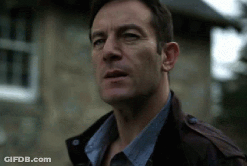 A Man Wearing A Leather Jacket And A Blue Shirt Is Standing In Front Of A Stone Building . GIF