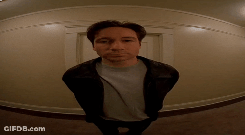 A Man Wearing A Leather Jacket And A Grey Shirt Stands In A Hallway GIF