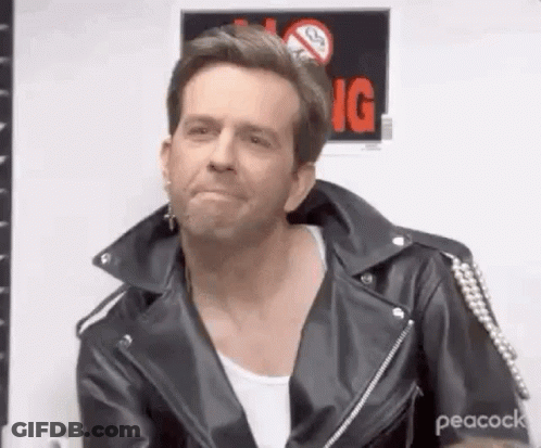 A Man Wearing A Leather Jacket And A White Shirt Is Sitting In Front Of A No Smoking Sign . GIF