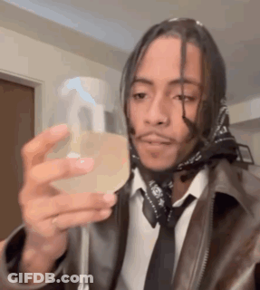 A Man Wearing A Leather Jacket And Tie Is Holding A Spray Bottle . GIF