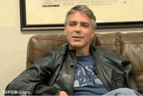 A Man Wearing A Leather Jacket Sits On A Couch In Front Of A Framed Picture That Says December GIF