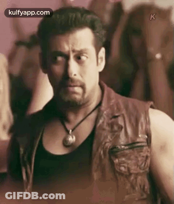 A Man Wearing A Leather Vest And A Necklace Is Standing In Front Of A Crowd Of People . GIF