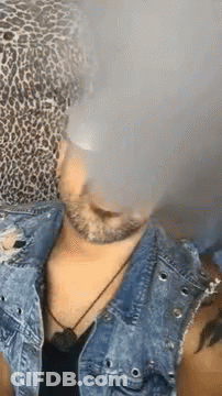 A Man Wearing A Leopard Print Hat And A Denim Jacket Is Smoking An Electronic Cigarette . GIF