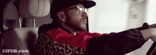 A Man Wearing A Leopard Print Jacket And Glasses Is Driving A Car GIF