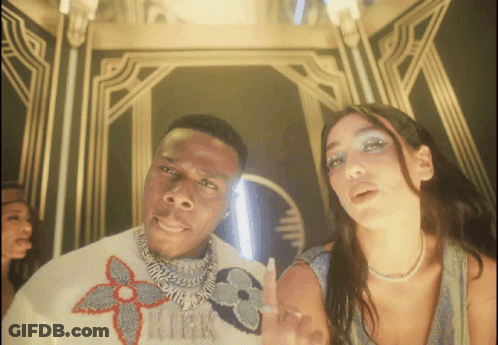 A Man Wearing A Louis Vuitton Sweater Stands Next To A Woman Wearing A Pearl Necklace GIF