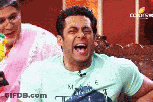 A Man Wearing A Make E T-Shirt Is Laughing While Sitting On A Couch GIF