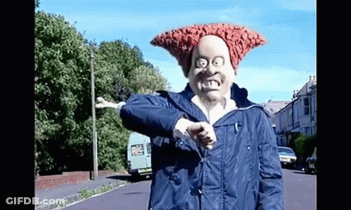 A Man Wearing A Mask And A Blue Jacket Is Giving A Thumbs Up While Standing On A Street . GIF