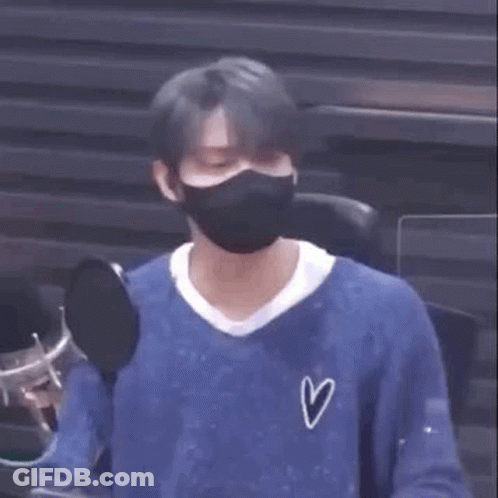 A Man Wearing A Mask And A Blue Shirt Is Sitting In Front Of A Microphone . GIF