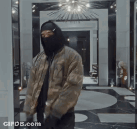 A Man Wearing A Mask And A Bomber Jacket Is Standing In A Room . GIF
