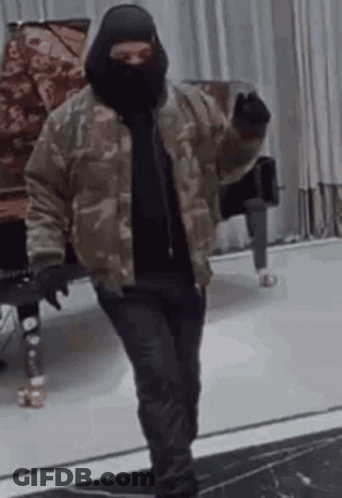 A Man Wearing A Mask And A Camouflage Jacket Is Standing In A Room . GIF