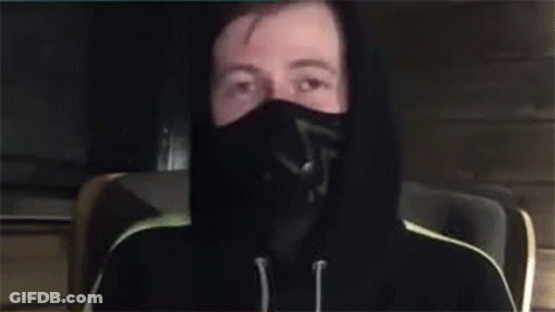 A Man Wearing A Mask And A Hoodie Is Waving His Hand . GIF