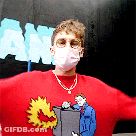 A Man Wearing A Mask And A Red Sweater With A Man Holding A Box GIF