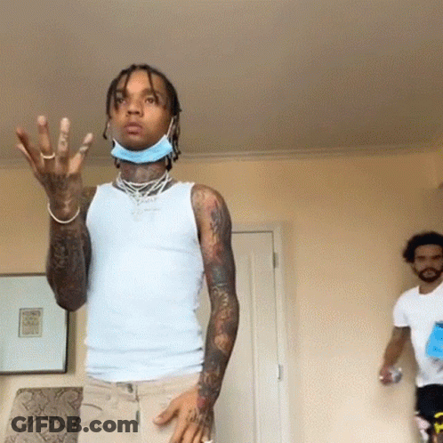 A Man Wearing A Mask And A White Tank Top Is Standing In A Room With Another Man . GIF