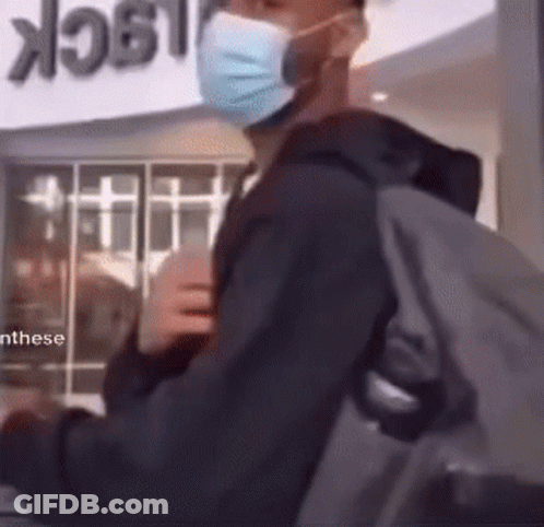 A Man Wearing A Mask And Carrying A Backpack Is Standing In Front Of A Sign That Says Lock GIF