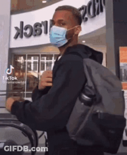 A Man Wearing A Mask And Carrying A Backpack Is Walking On An Escalator . GIF