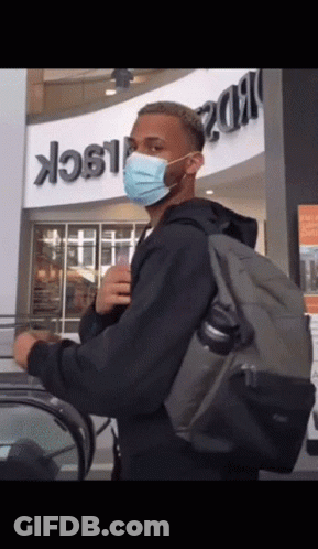 A Man Wearing A Mask And Carrying A Backpack Stands In Front Of A Building That Says Black GIF