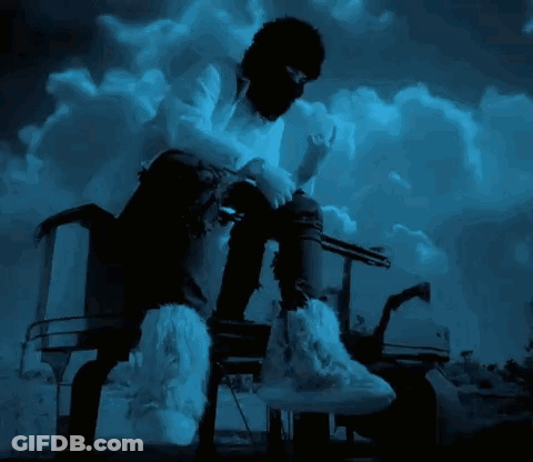 A Man Wearing A Mask And Furry Boots Is Sitting On A Chair GIF