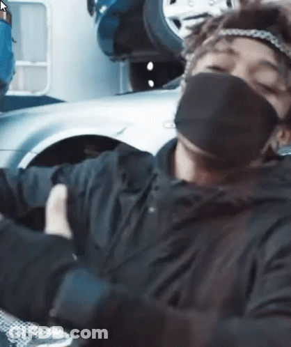 A Man Wearing A Mask And Gloves Is Sitting In Front Of A Car . GIF