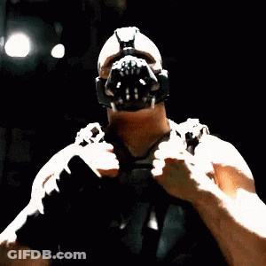 A Man Wearing A Mask And Gloves Is Standing In The Dark And Pointing At The Camera . GIF
