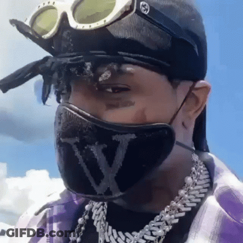 A Man Wearing A Mask And Goggles Is Wearing A Hat And A Necklace . GIF