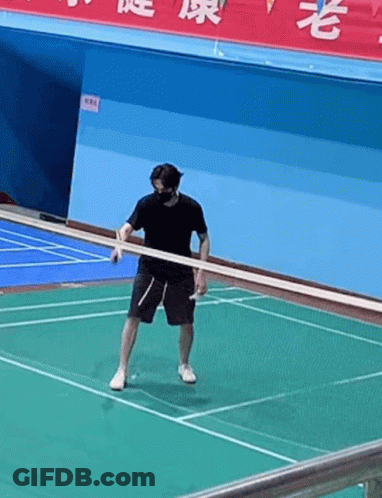 A Man Wearing A Mask Is Holding A Racket On A Badminton Court . GIF