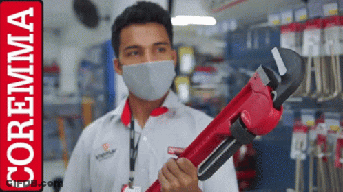 A Man Wearing A Mask Is Holding A Red Wrench In Front Of A Coremma Logo GIF