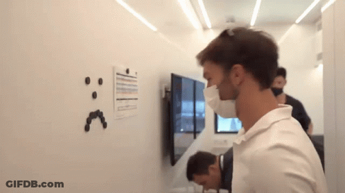 A Man Wearing A Mask Is Looking At A White Board With A Smiley Face Drawn On It GIF