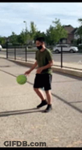 A Man Wearing A Mask Is Playing With A Ball On The Sidewalk GIF