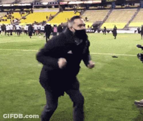 A Man Wearing A Mask Is Running On A Soccer Field . GIF