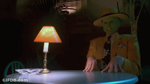 A Man Wearing A Mask Is Sitting At A Table With A Lamp On GIF