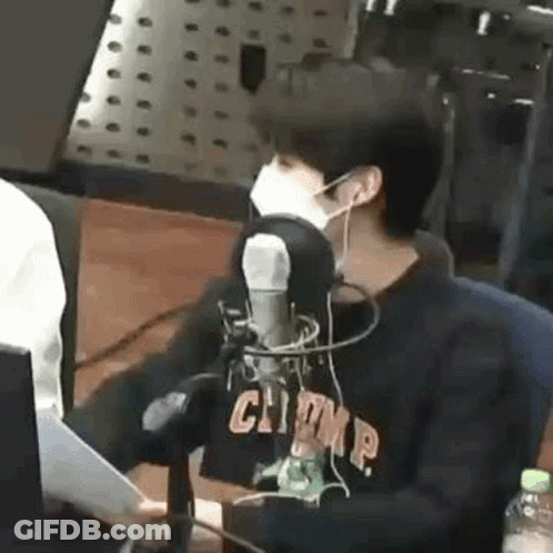 A Man Wearing A Mask Is Sitting In Front Of A Microphone In A Radio Station . GIF