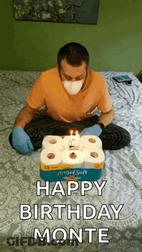 A Man Wearing A Mask Is Sitting On A Bed With A Birthday Cake Made Out Of Toilet Paper . GIF