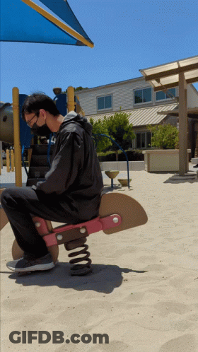 A Man Wearing A Mask Is Sitting On A Rocking Horse In The Sand GIF