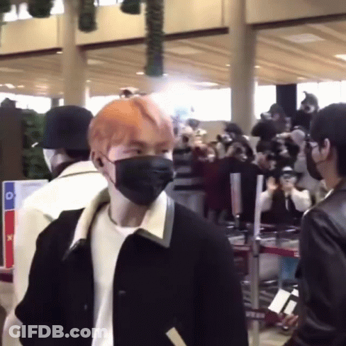 A Man Wearing A Mask Is Standing In Front Of A Crowd Of People At An Airport . GIF